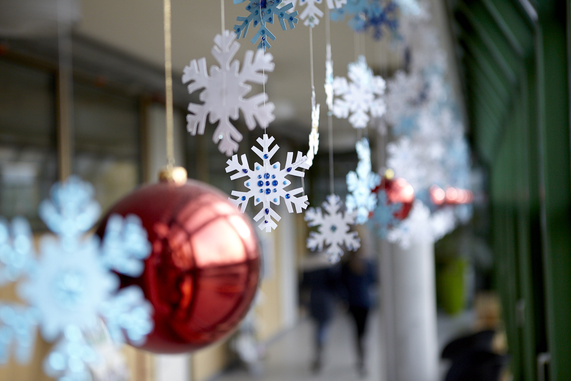 Hängende weiße und blaue Schneeflocken aus Papier und rote Weihnachtskugeln vor unscharfem Flur